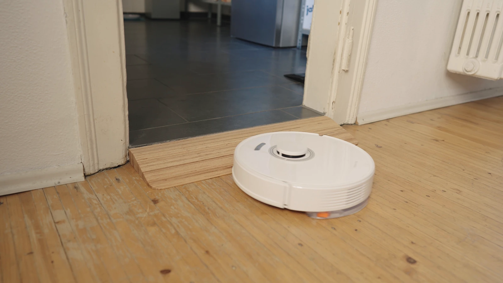 Robot aspirateur devant une rampe en bois dans un passage de porte