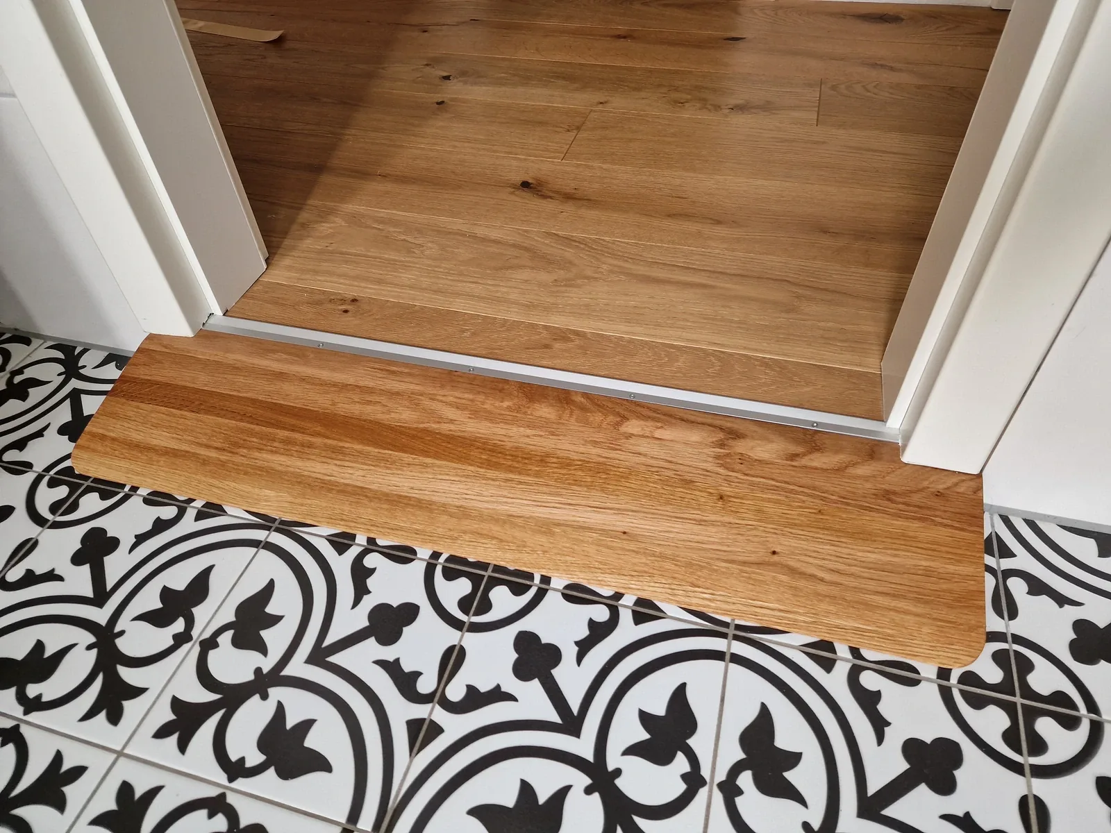 Rampe en bois avec plateforme passant sous un chambranle en saillie dans la pièce, sur un carrelage à motifs